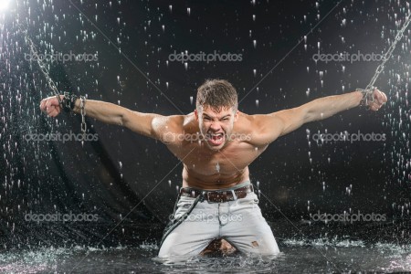 Strong man in chains posing under the rain, aqua studio